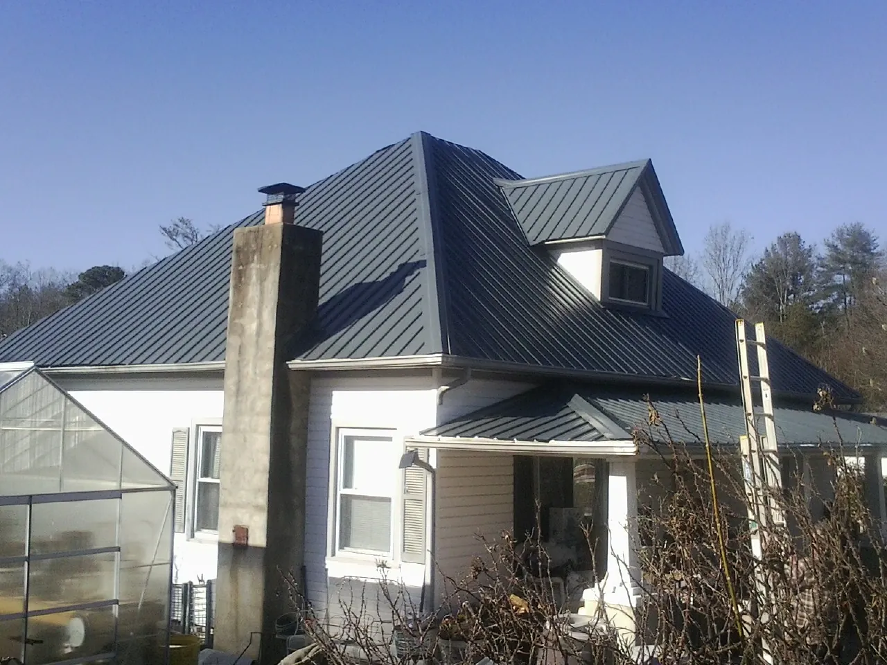 Dark blue standing seam metal roof on a white farmhouse with dormer — Slate & Tile Roof Repair by Roofing Brothers in Greenfield Center