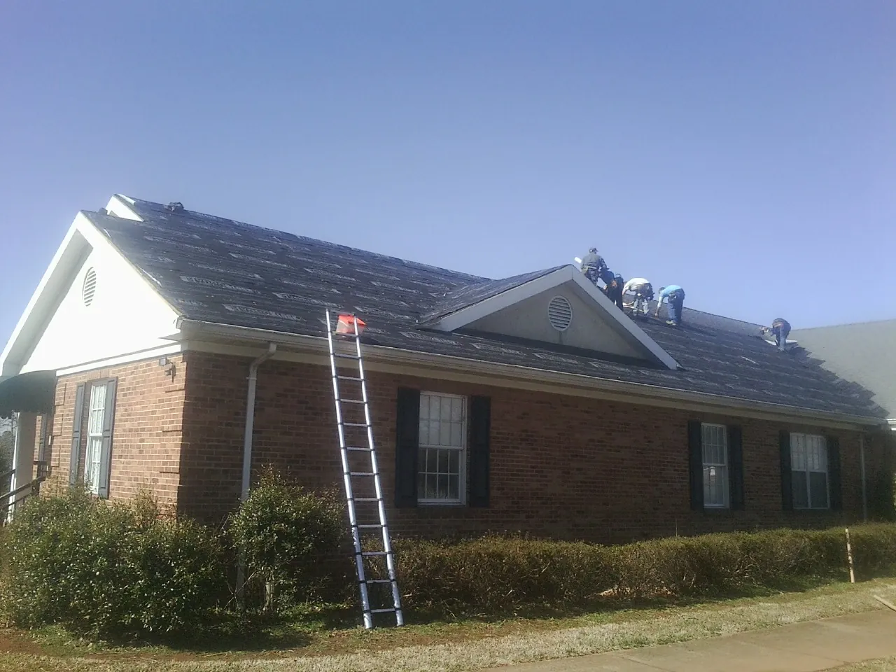 Crew tearing shingles off a brick ranch roof with a ladder set — Emergency Roof Repair work by our crew in Greenfield Center