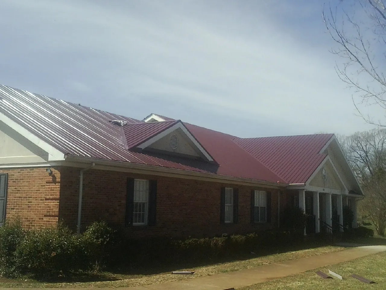 Red metal roof with gabled entries on a long brick building, from a Hail Damage Roof Repair job in Greenfield Center
