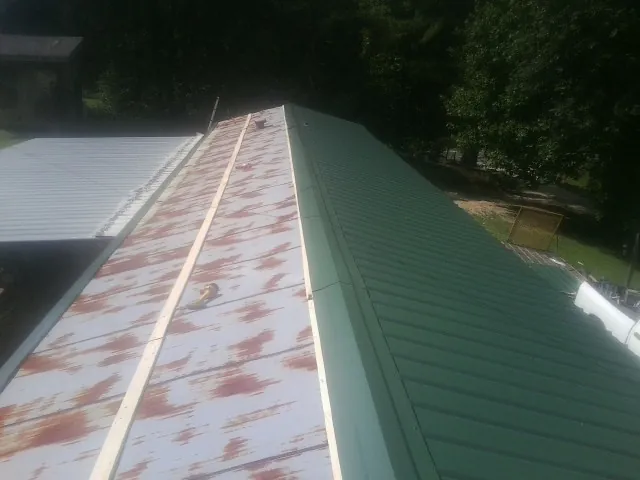 Old rusted panels beside newly installed green metal roofing — Wind Damage Roof Repair by Roofing Brothers in Greenfield Center