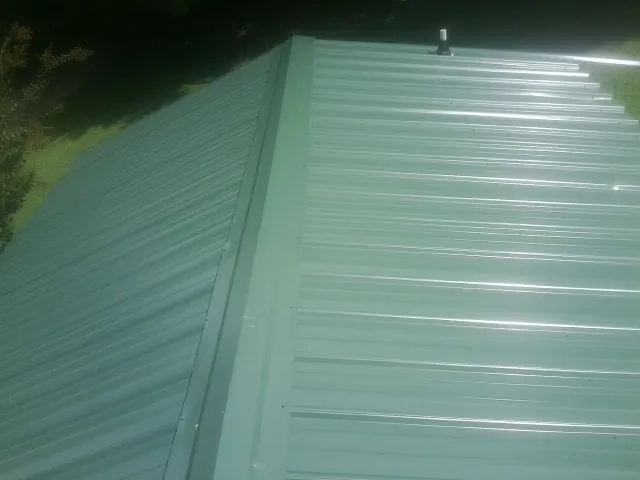 New green metal panels meeting at the ridge of a roof — Flat Roof Repair work by our crew in Greenfield Center