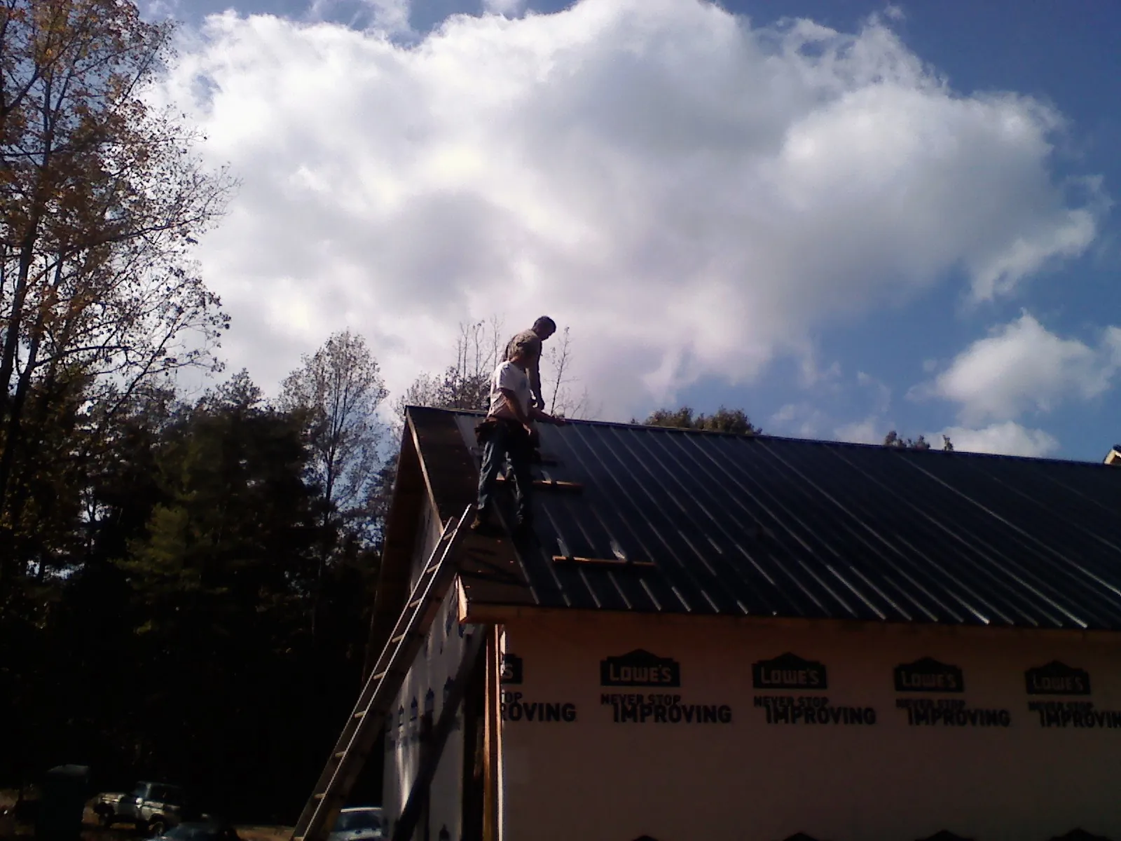 Roofer fastening dark metal panels high against a cloudy sky, from a Roof Inspection job in Greenfield Center