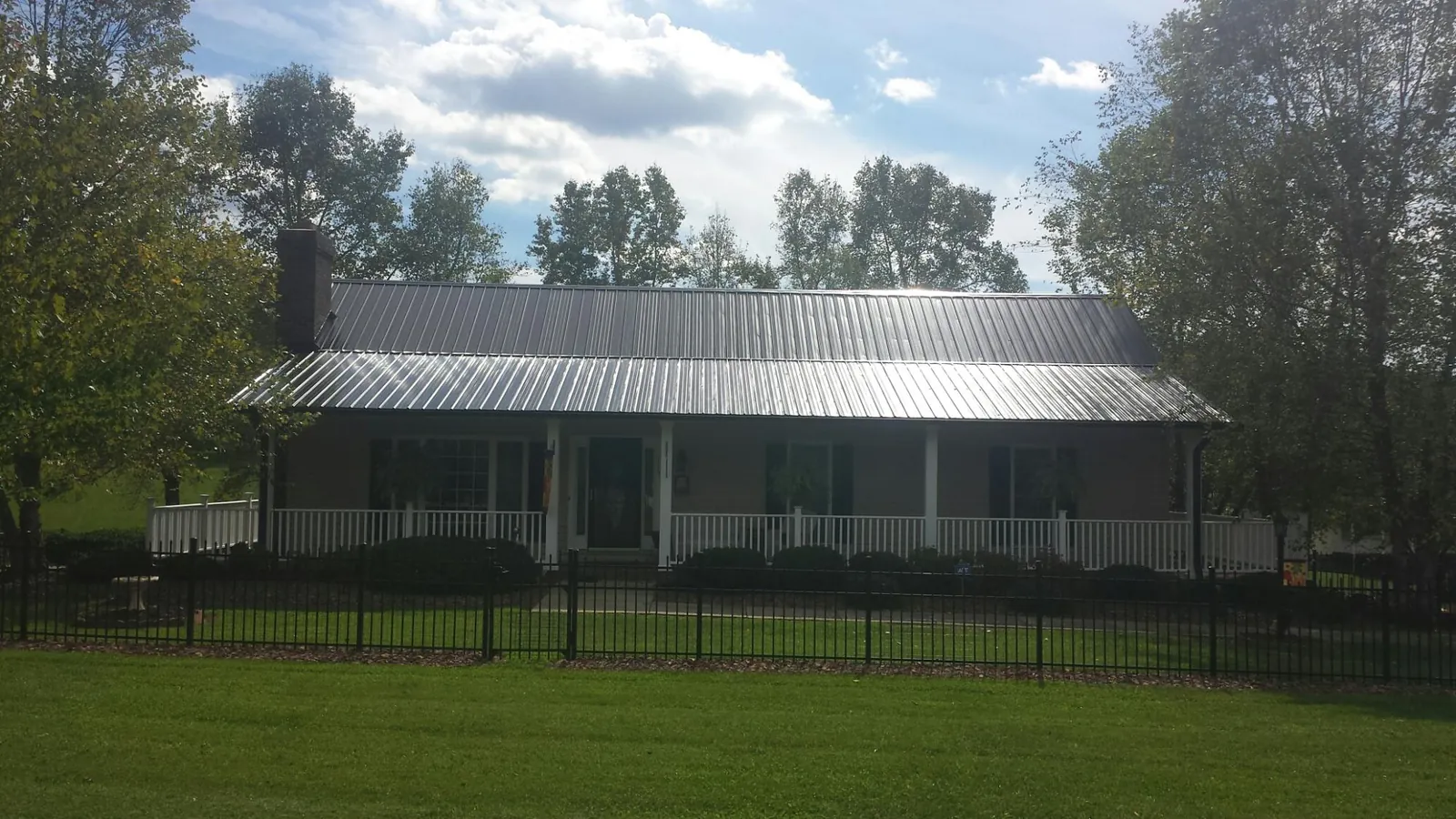 Gray metal roof on a brick ranch with a full width front porch — Gutter Guard Installation work by our crew in Greenfield Center
