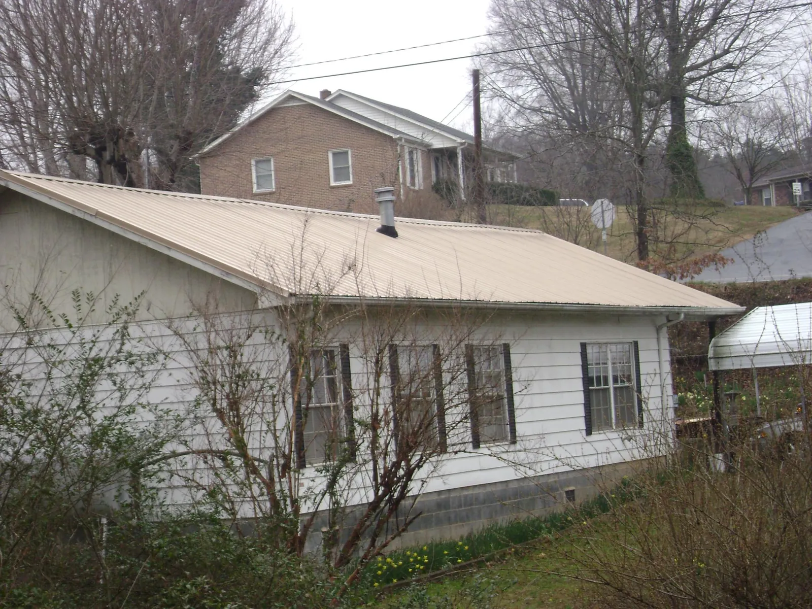 Tan metal roof on a white sided house set into a hillside — Commercial Roofing by Roofing Brothers in Greenfield Center