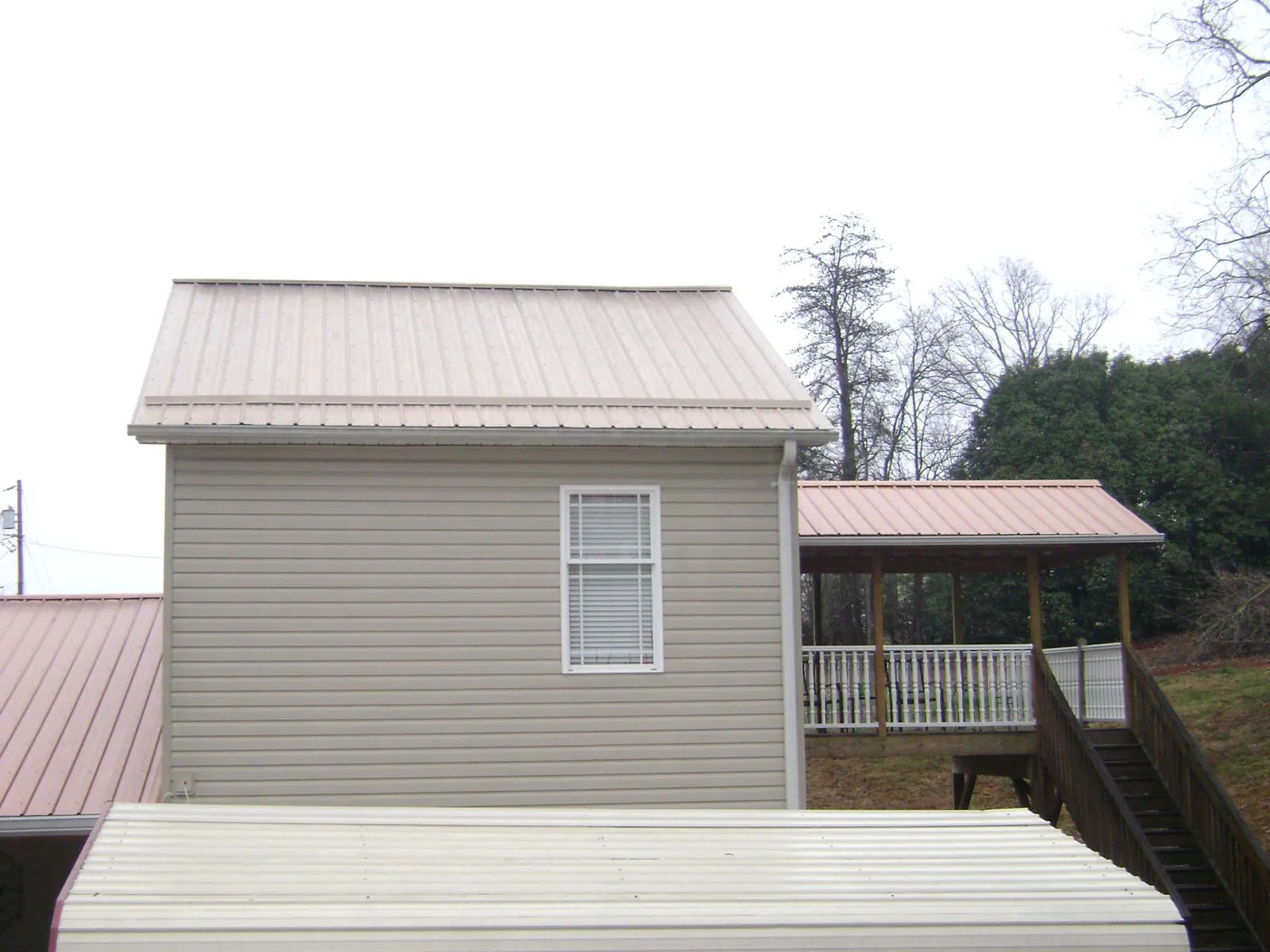 Tan metal roofs on a two story addition and attached porch, from a Roof Replacement job in Greenfield Center