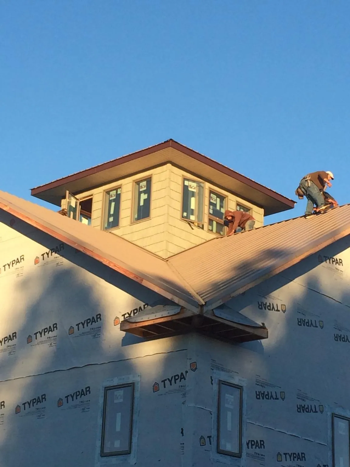 Roofers working around a rooftop cupola on a new metal roof at sunset — Roof Waterproofing in Greenfield Center by Roofing Brothers